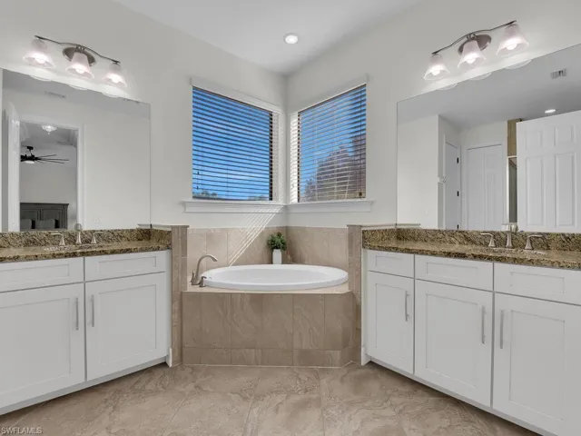 Bathroom featuring two vanities, a bath, and a ceiling fan