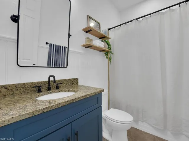 Bathroom featuring vanity, a wainscoted wall, light tile patterned floors, shower / bath combination with curtain, and a decorative wall