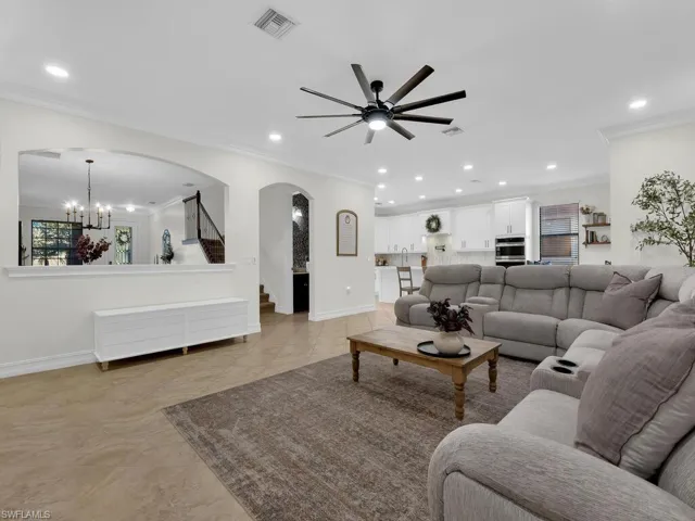 Living area featuring arched walkways, ornamental molding, a ceiling fan, and a chandelier