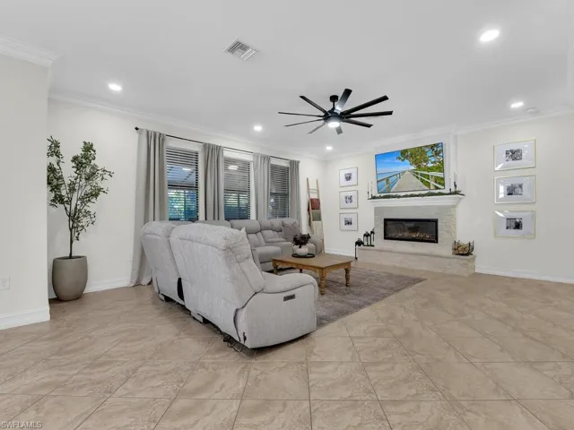Living area featuring ceiling fan, a glass covered fireplace, crown molding, and recessed lighting