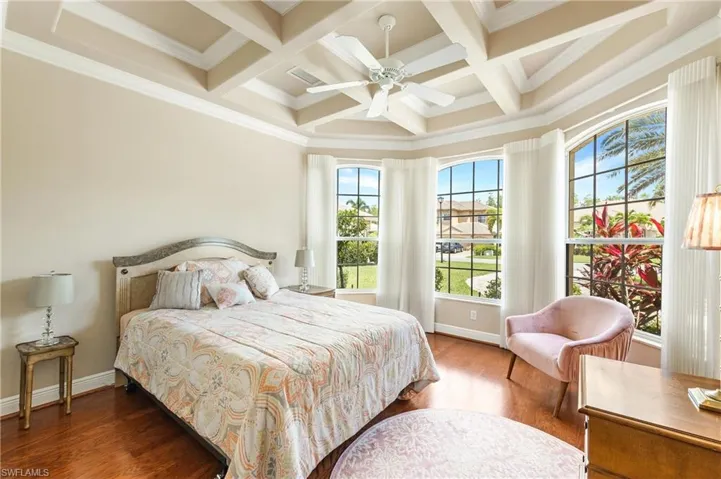 First floor Den being used as a Bedroom featuring hardwood flooring, a coffered ceiling with a ceiling fan, and a curved bay of three windows with arched transoms