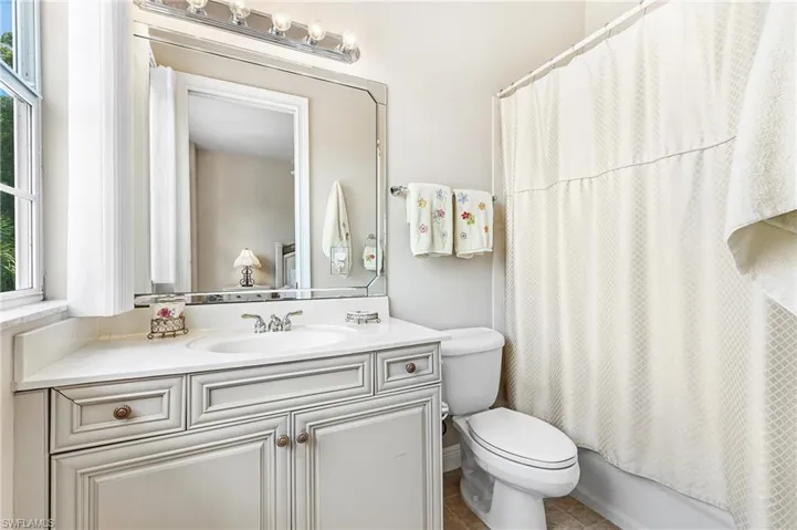 En-suite Bathroom featuring a single basin vanity with a light-colored countertop, an ornate framed mirror, and a shower/tub combination with a white curtain