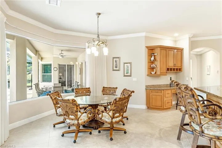 Dining area featuring a glass-top table, tile flooring, and a built-in wet bar with wood cabinetry and a stone-finish countertop
