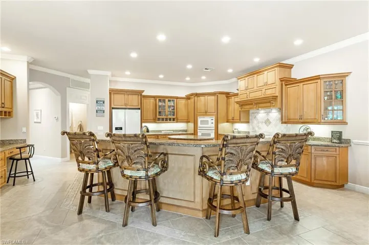 Spacious kitchen featuring breakfast bar, a large central island with seating, extensive wood cabinetry, light-toned countertops, tile backsplash, and recessed lighting