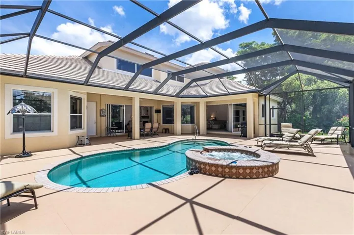 Screened lanai featuring a freeform swimming pool with an integrated spa, expansive deck, and a covered patio