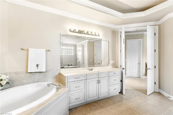 Spacious bathroom featuring a white soaking tub, an extensive white vanity with a light-colored countertop, and a large mirror with decorative lighting