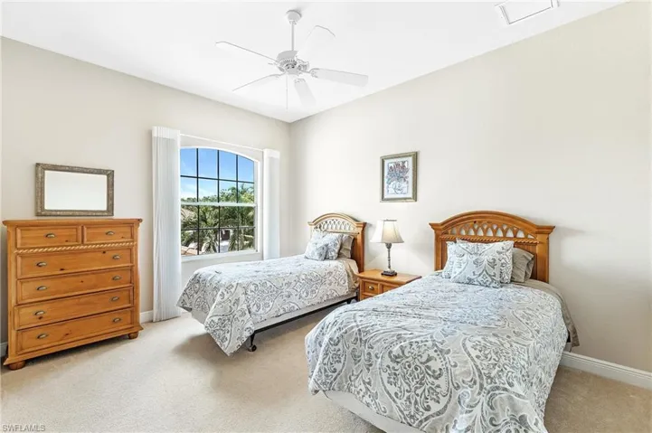 Upstairs bedroom with arched window with gridded panes, ceiling fan, neutral wall color, and wall-to-wall carpeting