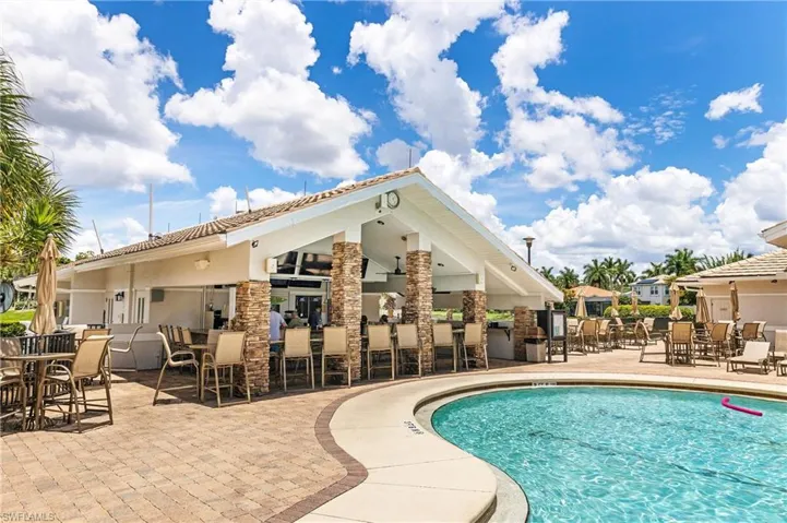 Expansive outdoor amenity area featuring a curvilinear swimming pool, a covered pavilion with a built-in bar, and extensive paver decking