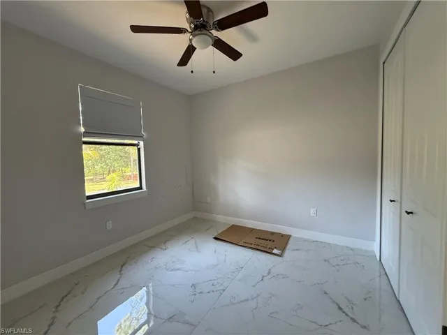 Interior room featuring large format tile flooring, a window with a roller shade, and a ceiling fan with integrated lighting
