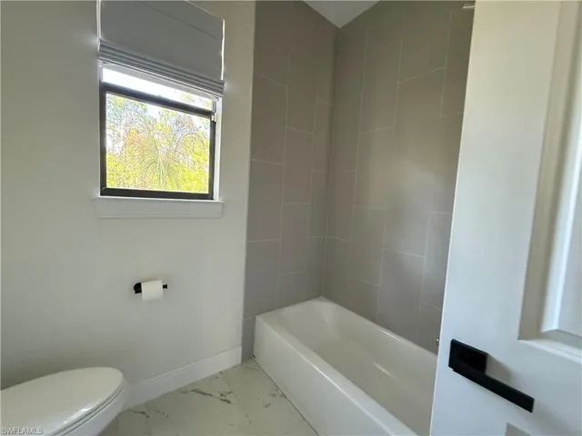 Bathroom featuring a white soaking tub, light gray subway tile surround, and a white toilet