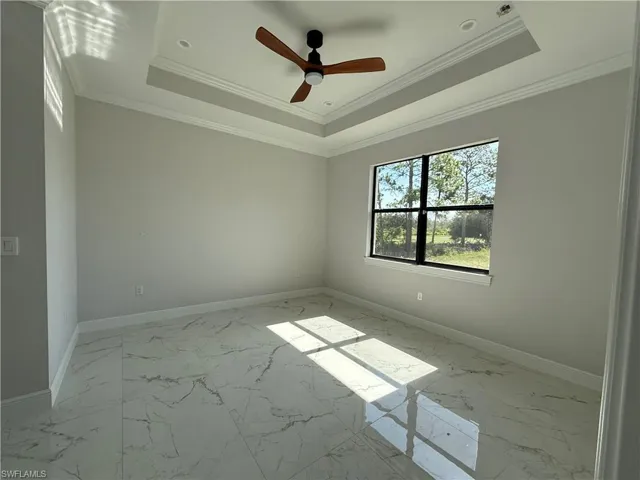 Spacious room featuring tray ceiling with crown molding, recessed lighting, and a ceiling fan