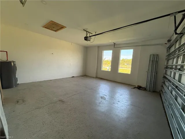 Spacious garage featuring a durable concrete floor, three windows providing natural light, an overhead garage door opener, and attic access