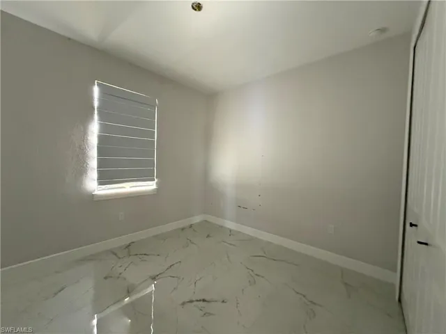 Room featuring white walls with white baseboards, a window with horizontal blinds, and a white tile floor with gray veining