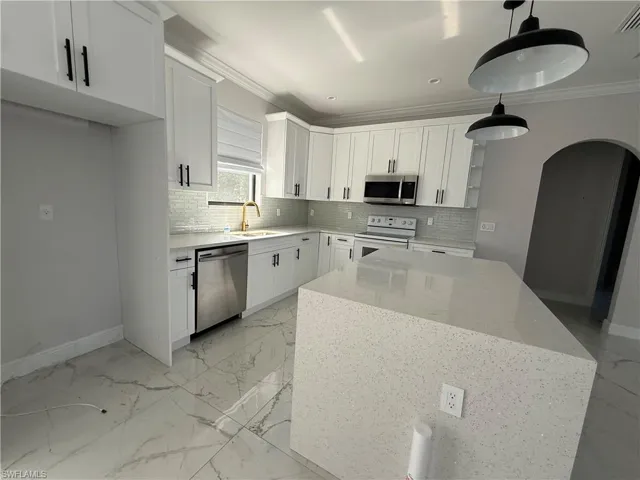Modern kitchen featuring white shaker cabinetry, stainless steel appliances, a white tile backsplash, a large kitchen island with a light-colored countertop, and two pendant light fixtures