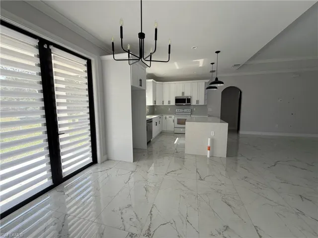 Bright open-concept kitchen featuring white shaker cabinetry, stainless steel appliances, and a central island with a light-toned countertop