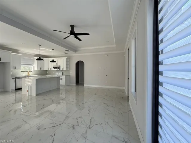 Spacious open concept living area featuring large format marble-look tile flooring, a modern kitchen island with pendant lighting, white shaker cabinetry, and a ceiling fan