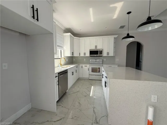 Modern kitchen featuring white shaker cabinetry with black hardware, stainless steel appliances, and a light-toned backsplash