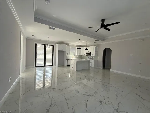 Spacious open-concept living area featuring large format tile flooring, crown molding, and a modern kitchen with white cabinetry