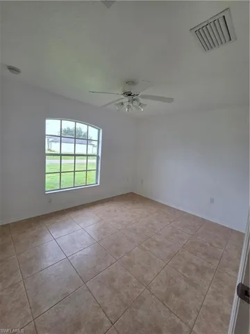 Arched window with gridded panes, ceiling fan with integrated lighting, and neutral-toned tile flooring