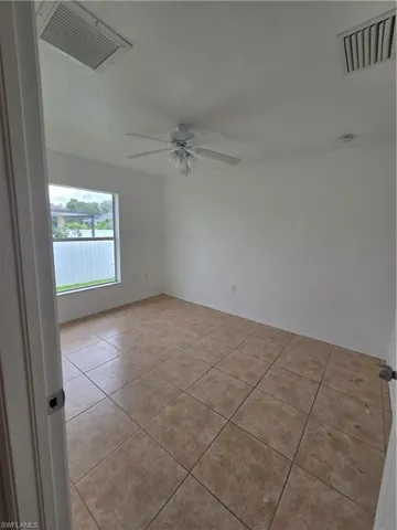 Neutral-toned tile flooring, white painted walls, and a ceiling fan with integrated lighting