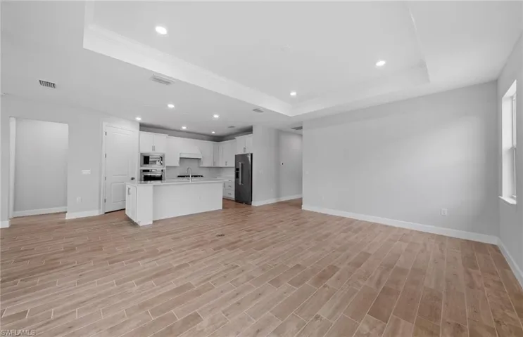 Unfurnished living room featuring a raised ceiling, light hardwood / wood-style floors, and sink