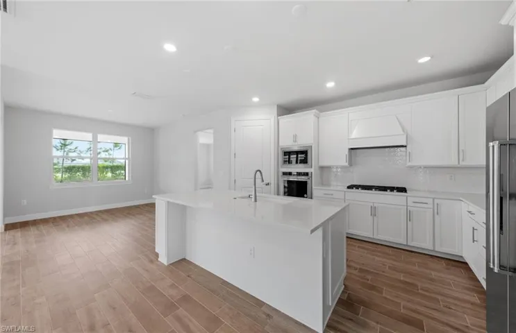 Kitchen with appliances with stainless steel finishes, white cabinetry, an island with sink, premium range hood, and sink