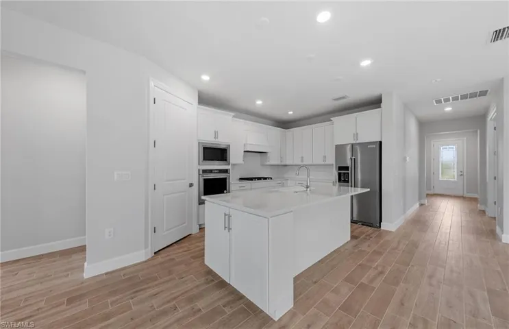 Kitchen with white cabinets, an island with sink, stainless steel appliances, and light wood-type flooring