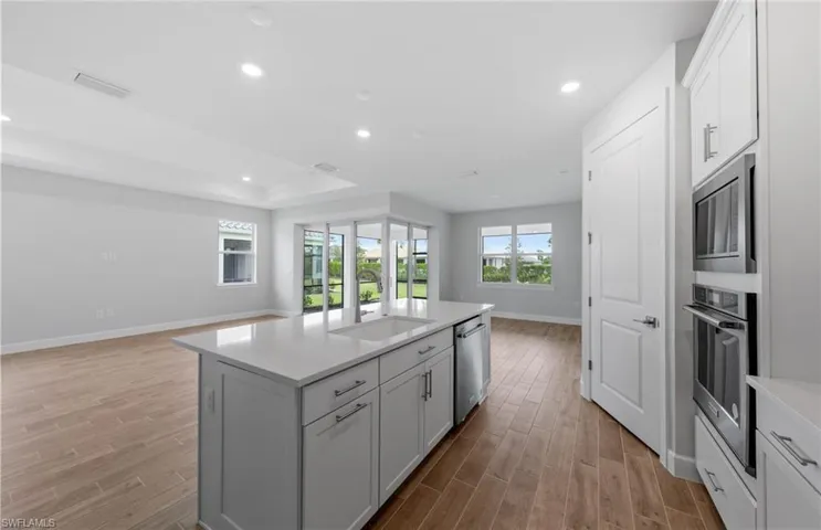 Kitchen with sink, a kitchen island with sink, light hardwood / wood-style flooring, a tray ceiling, and appliances with stainless steel finishes