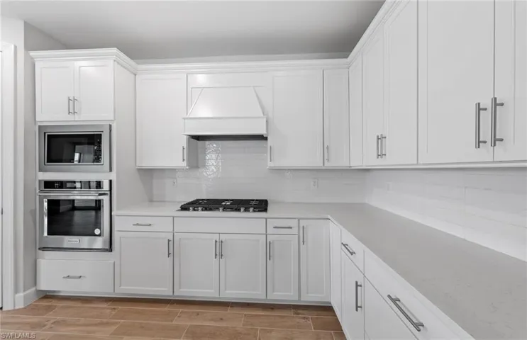 Kitchen with white cabinets, appliances with stainless steel finishes, custom range hood, and tasteful backsplash