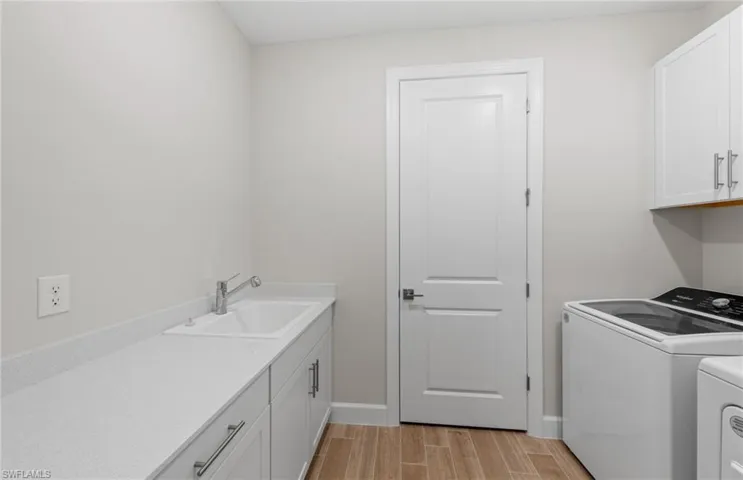 Clothes washing area featuring light hardwood / wood-style floors, sink, washer and dryer, and cabinets