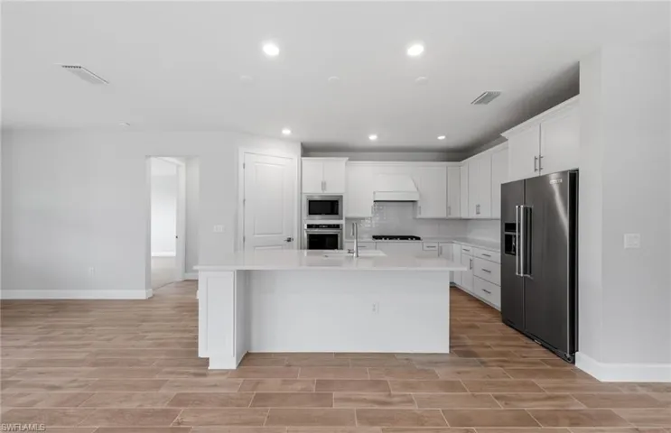 Kitchen featuring white cabinets, a kitchen island with sink, appliances with stainless steel finishes, and custom range hood