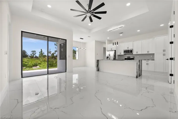 Unfurnished living room with a tray ceiling, light marble finish floors, ceiling fan, and recessed lighting