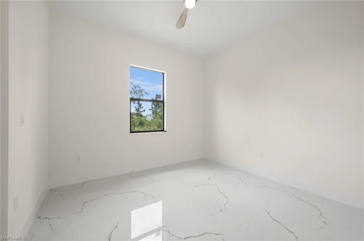 Unfurnished room with marble look tile flooring and ceiling fan