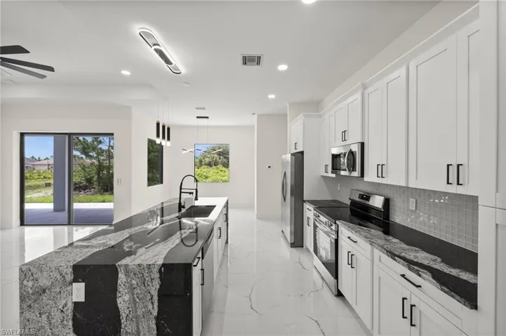 Kitchen featuring appliances with stainless steel finishes, recessed lighting, tasteful backsplash, light marble finish floors, and an island with sink