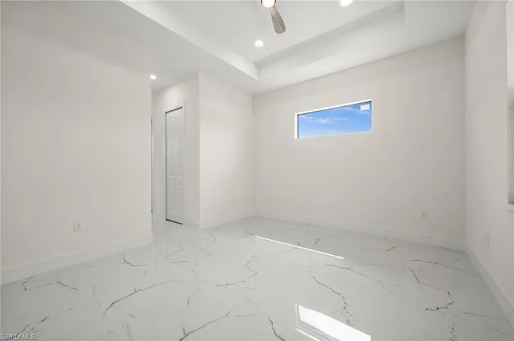 Unfurnished room featuring light marble finish floors, recessed lighting, a tray ceiling, and a ceiling fan