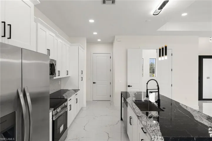 Kitchen featuring appliances with stainless steel finishes, recessed lighting, light marble finish floors, white cabinetry, and dark stone counters