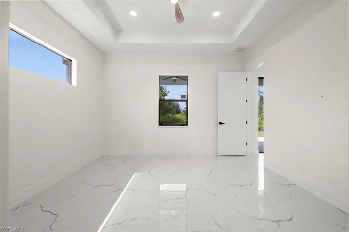 Empty room with healthy amount of natural light, marble tiled flooring, a tray ceiling, and recessed lighting