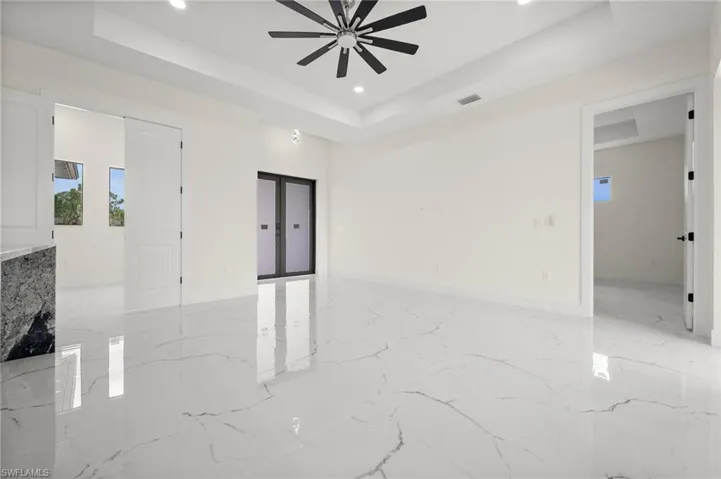 Empty room with a raised ceiling, recessed lighting, a ceiling fan, and light marble finish floors