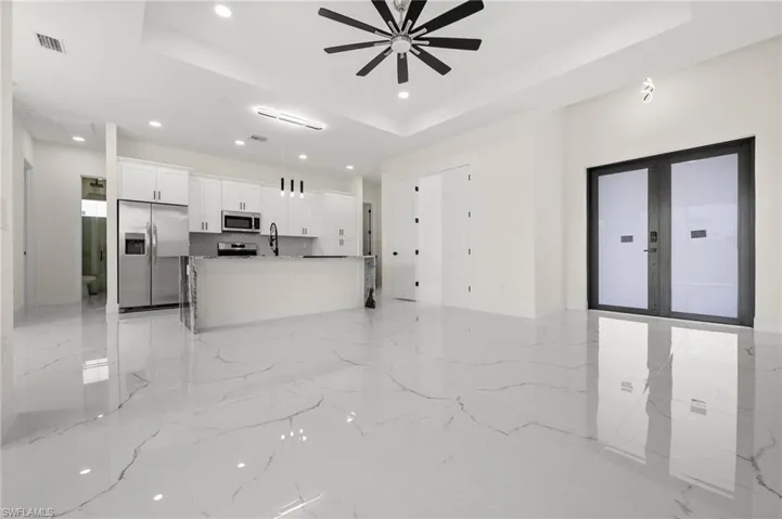 Unfurnished living room featuring a tray ceiling, recessed lighting, ceiling fan, light marble finish flooring, and french doors