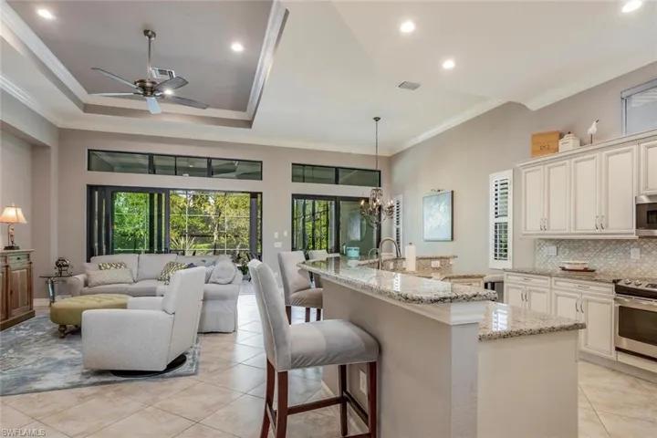 Kitchen with a breakfast bar, tasteful backsplash, light stone countertops, ornamental molding, and a kitchen island with sink