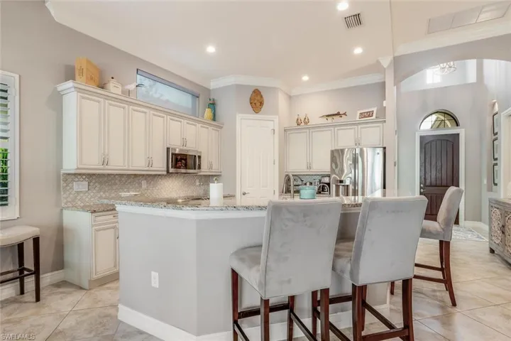 Kitchen featuring granite countertops, ceramic tile backsplash, stainless steel appliances, and a kitchen breakfast bar