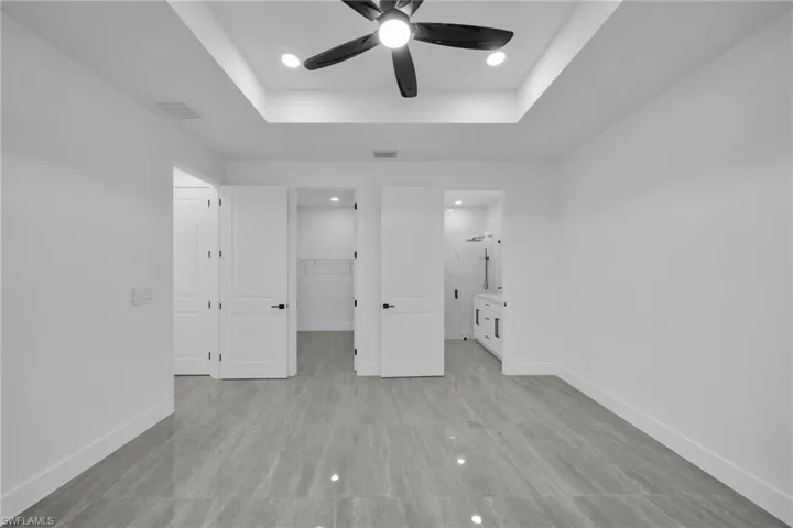 Unfurnished bedroom with a walk in closet, a raised ceiling, recessed lighting, a ceiling fan, and connected bathroom