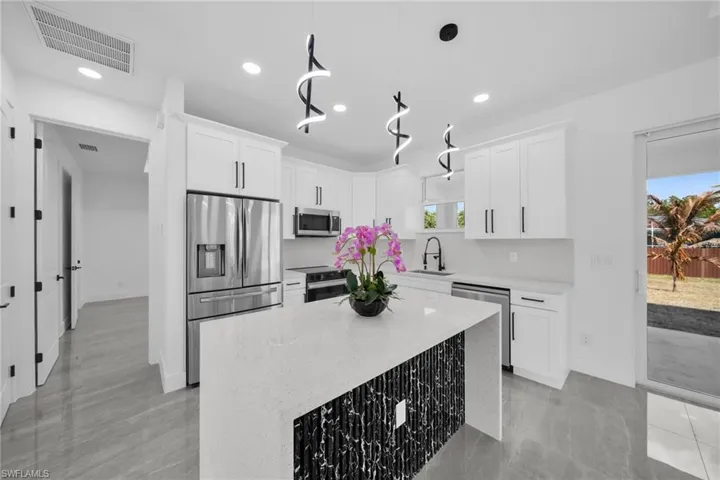 Kitchen featuring a center island, stainless steel appliances, light stone countertops, white cabinets, and decorative light fixtures