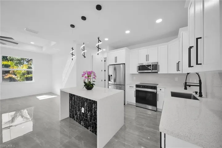 Kitchen with stainless steel appliances, white cabinets, hanging light fixtures, light stone countertops, and backsplash