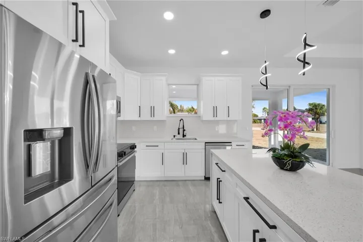 Kitchen featuring stainless steel appliances, white cabinets, light stone countertops, pendant lighting, and backsplash