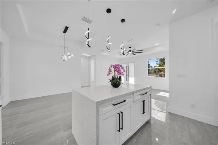 Kitchen featuring white cabinetry, hanging light fixtures, light stone countertops, a center island, and open floor plan