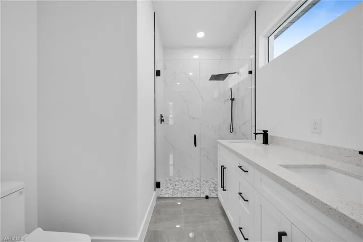 Bathroom featuring a marble finish shower, double vanity, and recessed lighting