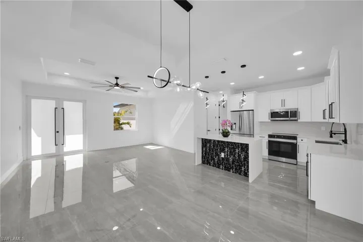 Kitchen featuring stainless steel appliances, light stone counters, open floor plan, white cabinets, and pendant lighting