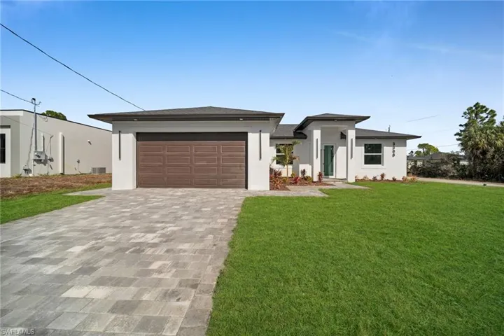 Prairie-style home with stucco siding, decorative driveway, a front yard, and an attached garage