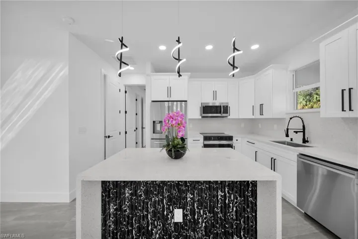 Kitchen with stainless steel appliances, light stone counters, white cabinets, and a center island